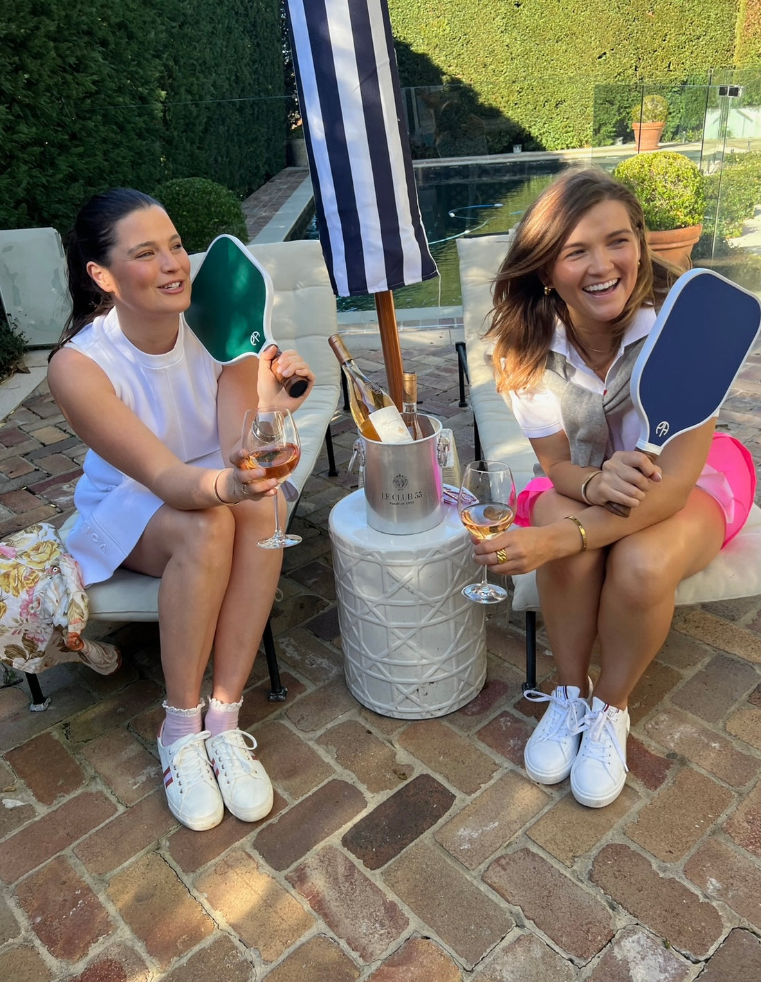 Two girls drinking rose by the pool holding pickleball paddles