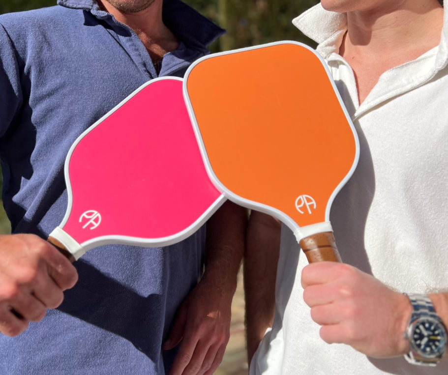 Two men holding a pink and orange pickleball paddle.