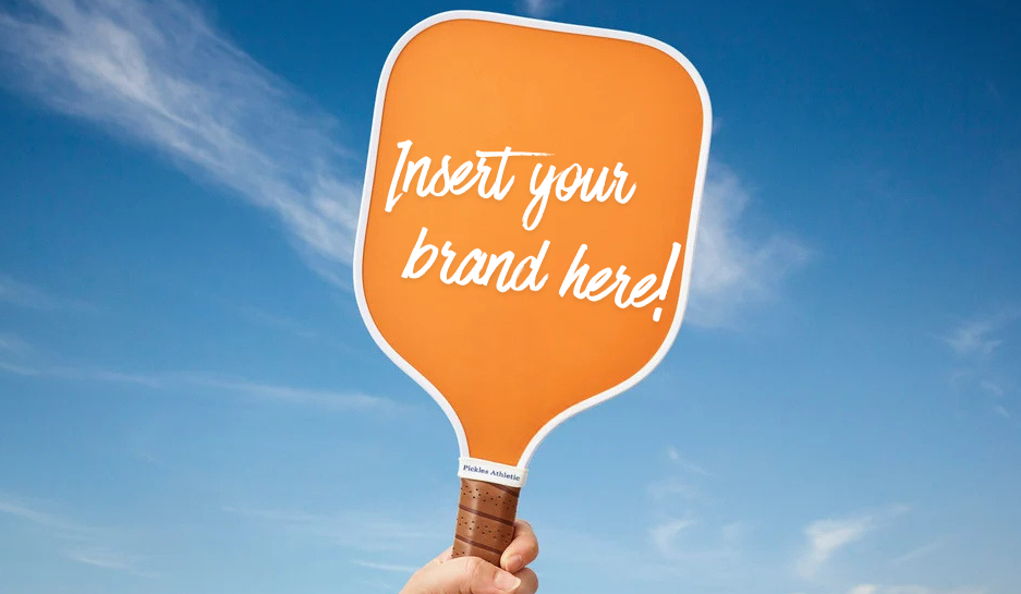 An orange paddle-shaped sign held by a hand against a blue sky with clouds, featuring the text 'Insert your brand here!' in white script.